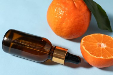 Aromatik mandalina yağı şişede ve narenciye meyveleri açık mavi masada, yakın plan.