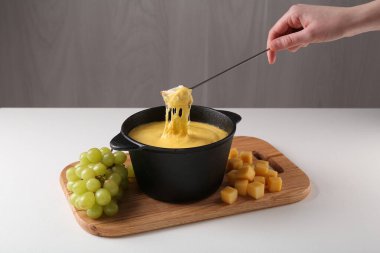 Beyaz masada eritilmiş peynirle fondü kabına bir parça ekmek daldıran bir kadın.