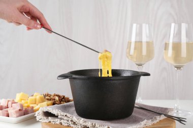 Bir parça jambonu fondü kabına daldırıp masada erimiş peynirle, yakın plan.