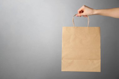 Gri arka planda Kraft kağıt çantası tutan bir kadın, mesaj için yeri olan yakın plan. Tasarım için model