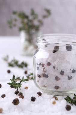 Cam kavanozda biberli tuz ve beyaz masada kekik, yakın plan.