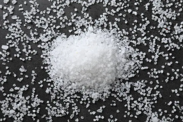 Heap of natural salt on black table, top view