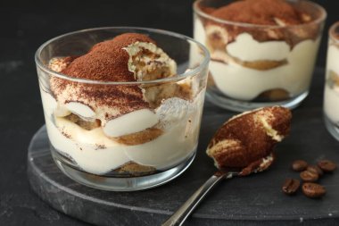 Siyah masada bardaklarda, kaşıklarda ve kahve çekirdeklerinde nefis tiramisu, yakın plan.