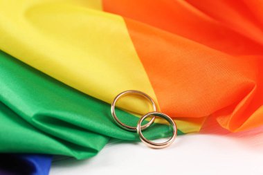 Gökkuşağı LGBT bayrağı ve alyanslar beyaz ahşap masada, yakın plan
