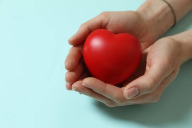 Açık mavi arka planda kırmızı dekoratif kalp taşıyan kadın, yakın plan. Metin için boşluk