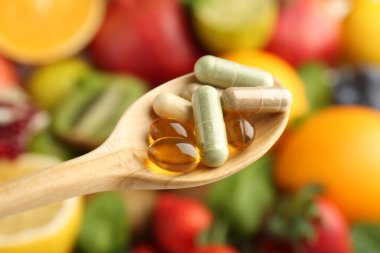 Kaşık içinde farklı vitamin hapları taze meyvelerin üzerinde, yakın çekim