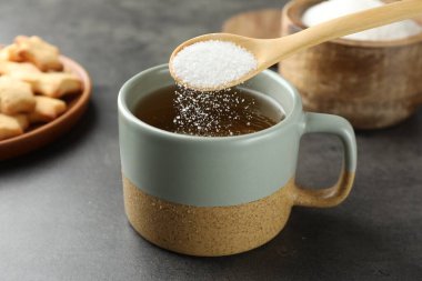 Gri masada aromatik çaya şeker ekleniyor, yakın plan.