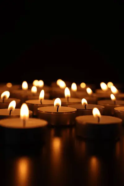 Burning candles on dark surface against black background