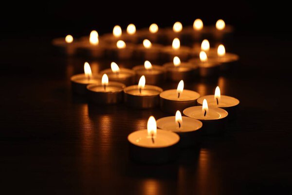 Burning tealight candles on dark surface, closeup
