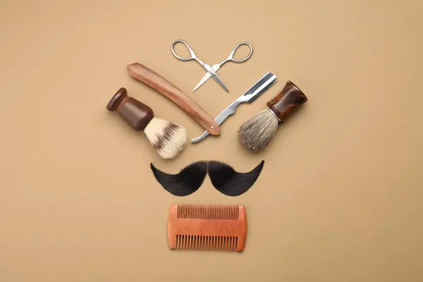 Artificial moustache and barber tools on beige background, flat lay