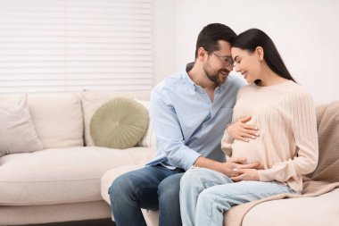Kocasıyla evdeki koltukta oturan mutlu hamile kadın, mesaj atmak için yer var.