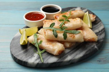 Lezzetli kızarmış börek, roka, limon ve soslar açık mavi ahşap masada, yakın plan.