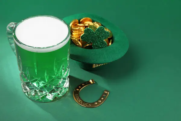 St. Patrick\'s day party. Green beer, leprechaun hat with gold, horseshoe and decorative clover leaf on green background. Space for text