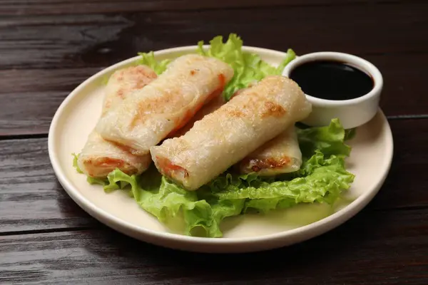 Delicious fried spring rolls with soy sauce on wooden table, closeup