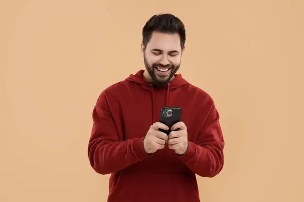 stock image Happy young man using smartphone on beige background