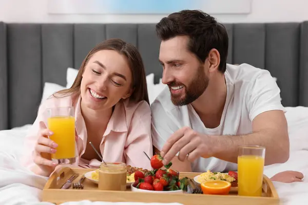 Happy couple eating tasty breakfast on bed at home