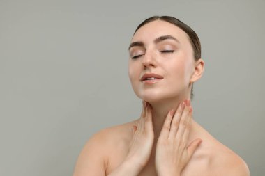 Gri arka planda boynuna dokunan güzel bir kadın. Metin için boşluk