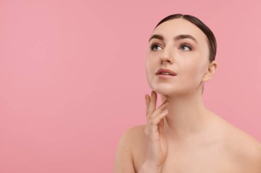 Güzel bir kadın pembe arka planda boynuna dokunuyor. Metin için boşluk