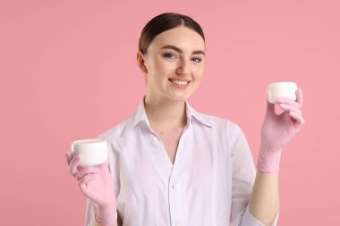 Pembe arka planda kozmetik ürünleri olan bir kozmetikçi.