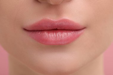 Pembe arka planda güzel dolgun dudakları olan genç bir kadın, yakın plan.