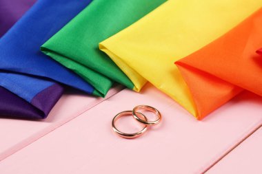 Gökkuşağı LGBT bayrağı ve alyanslar pembe ahşap masada, yakın plan.