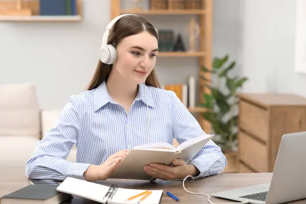 stock image E-learning. Young woman with book during online lesson at table indoors