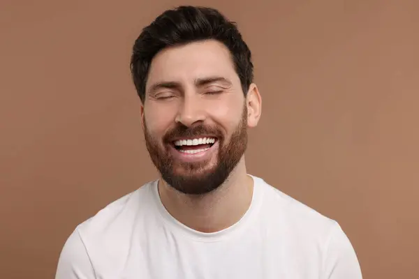 Handsome man laughing on light brown background, closeup