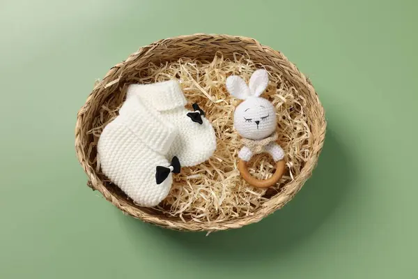 Different baby accessories in wicker box on green background, top view