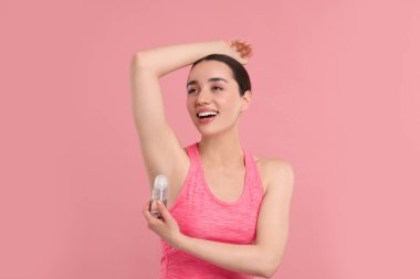Güzel bir kadın pembe arka plana deodorant sürüyor.