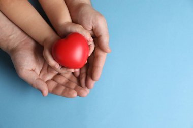 Baba ve çocuğu açık mavi arka planda kırmızı dekoratif kalp taşıyorlar. Metin için boşluk