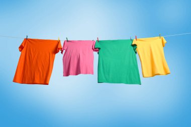 Mavi gökyüzüne karşı çamaşır ipinde kuruyan renkli tişörtler, düşük açılı görünüm.