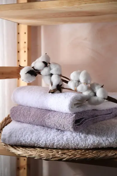 Stacked soft towels and cotton branch on shelf indoors
