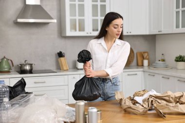 Çöp ayıklama. Mutfaktaki masada plastik çantalı kadın.