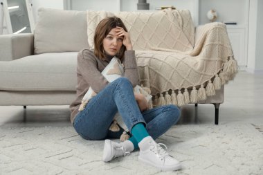 Üzgün genç kadın evde yerde oturuyor.