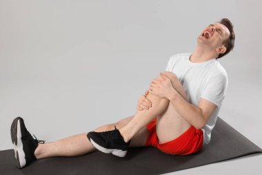 Bacak ağrısı çeken bir adam gri arka planda.