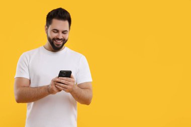 Mutlu genç adam sarı arka planda akıllı telefon kullanıyor, mesaj için boşluk