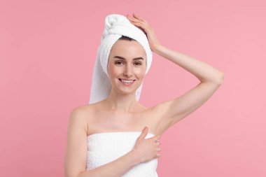 Güzel bir kadın pembe arka planda pürüzsüz, temiz bir ciltle koltukaltı gösteriyor.