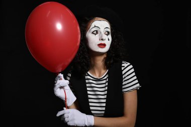 Siyah arka planda balon pozu veren pandomim kostümlü genç bir kadın.
