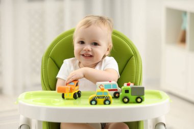Çocuk oyuncakları. Evdeki yüksek sandalyede oyuncak arabalarla oynayan sevimli küçük çocuk.