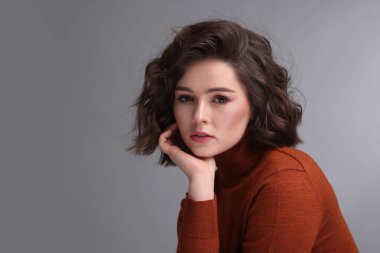 Gri arka planda dalgalı saç stili olan güzel bir genç kadının portresi. Metin için boşluk