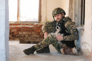 Terk edilmiş binada başıboş köpekle oturan Ukraynalı asker.