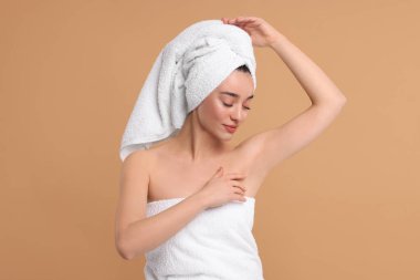 Güzel bir kadın bej arka planda pürüzsüz, temiz bir ciltle koltukaltı gösteriyor.