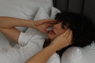 Geceleri yatakta baş ağrısı çeken genç bir kadın.