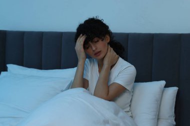 Geceleri yatakta baş ağrısı çeken genç bir kadın.
