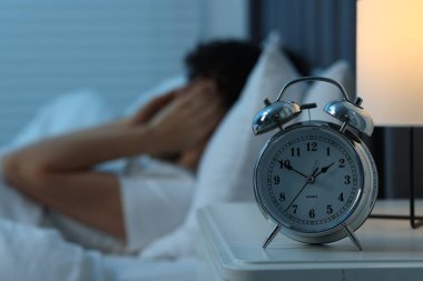 Gece yatakta baş ağrısı çeken kadın, çalar saate odaklan.