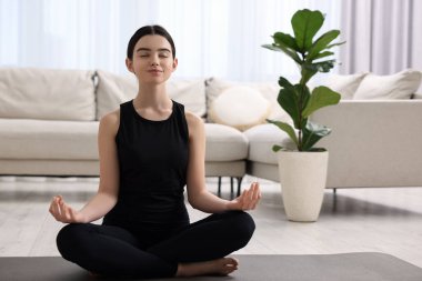 Evde yoga minderi üzerinde meditasyon yapan güzel bir kız.