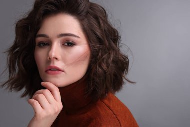 Gri arka planda dalgalı saç stili olan güzel bir genç kadın. Metin için boşluk