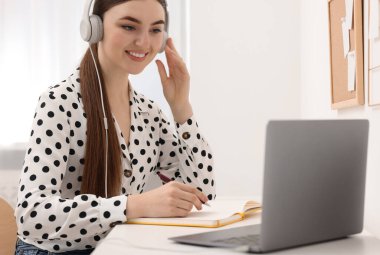 E-öğrenme. İçerideki masada online ders sırasında dizüstü bilgisayar kullanan genç bir kadın.