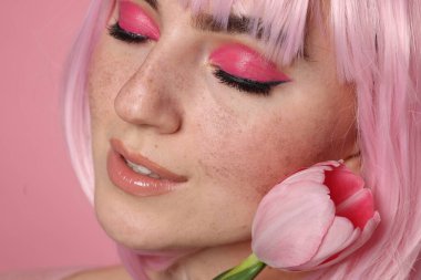 Parlak makyajlı güzel bir kadın, sahte çiller ve pembe arka planda lale, yakın plan.