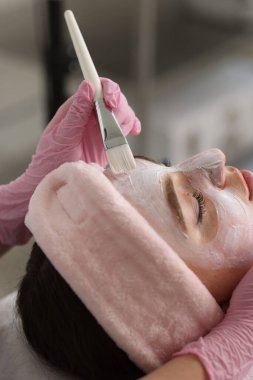 Kozmetik uzmanı klinikte kadının yüzüne maske takıyor.